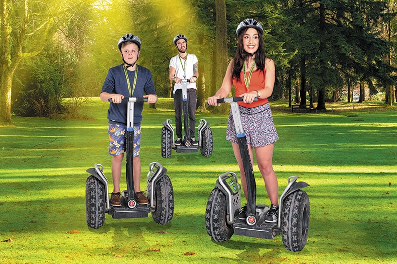 A woman, boy and man on segways in a sunny forest.