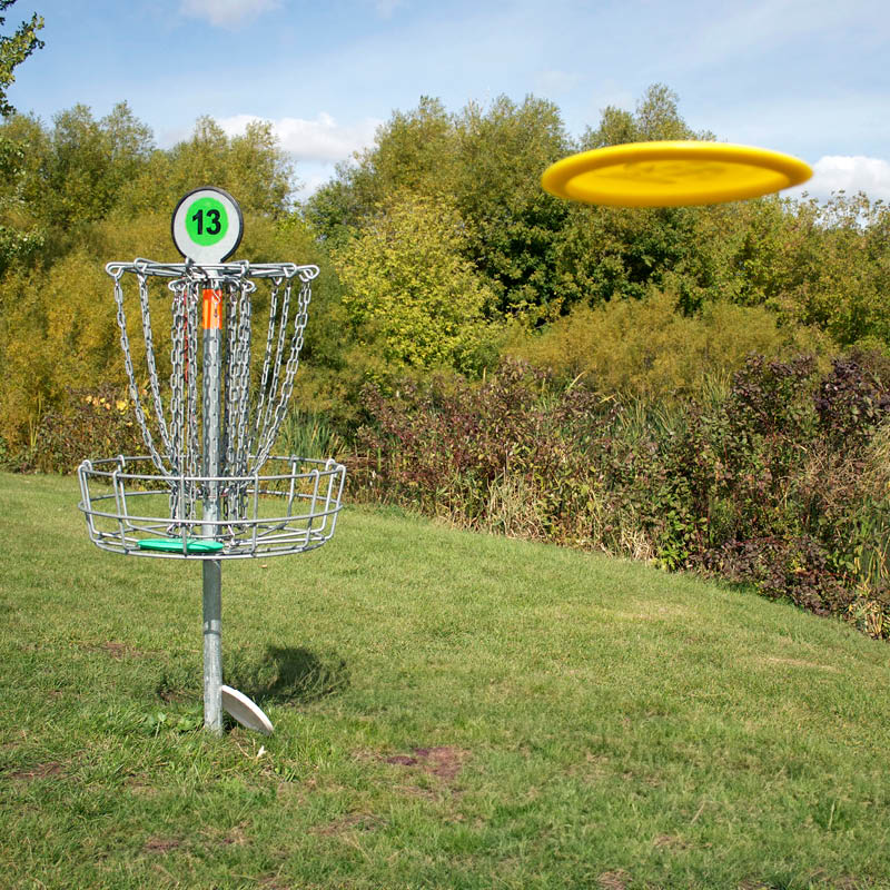 A disc golf frisbee flying in the air at the hole.
